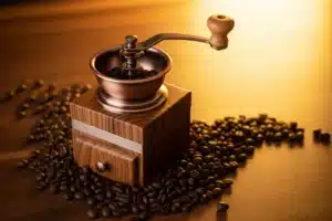 Moulin à café artisanal en bois et métal entouré de grains de café torréfiés, lumière dorée