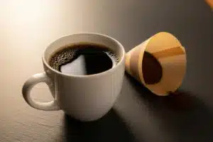 Tasse de café filtre blanc posée sur ardoise grise avec filtre en papier