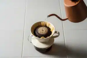Dripper V60 Hario en céramique sur comptoir clair, versement d'eau en spirale lors du bloom