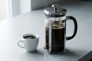Cafetière à piston sur plan de travail gris clair, tasse blanche à côté